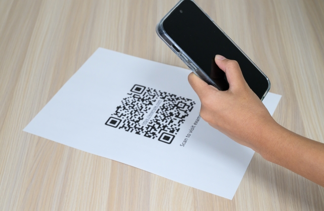 紙のチラシに印刷されたQRコードをスマートフォンで読み取る様子